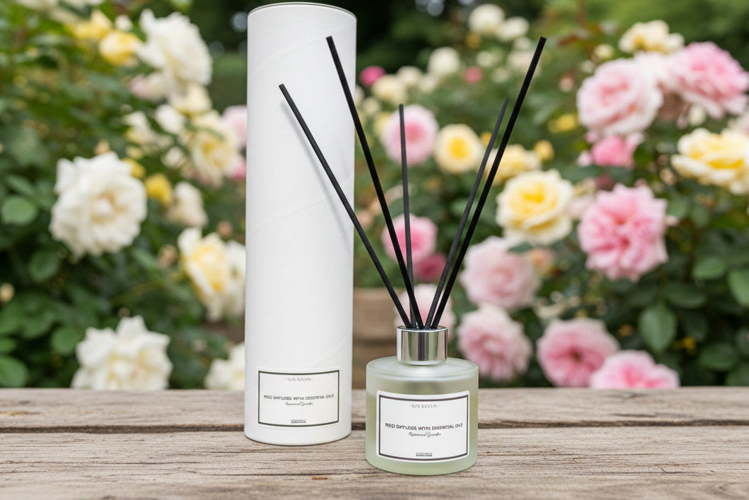 Diffuser with reeds and bottle on a wooden surface with flowers in the background