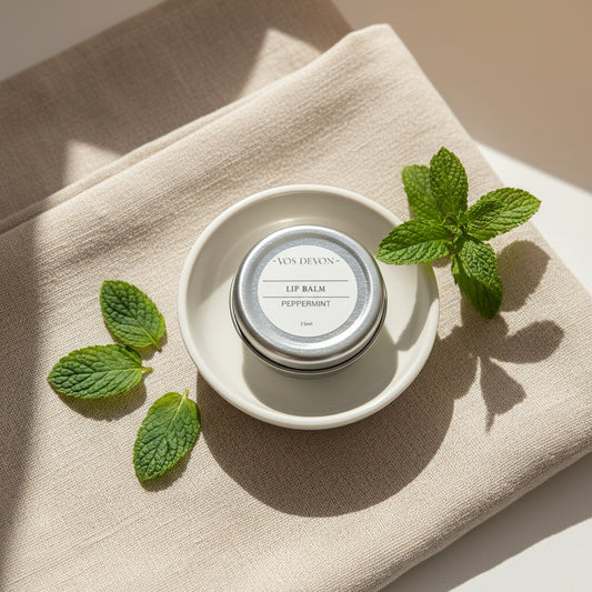 small round silver metal tin of VOS DEVON lip balm, labelled Peppermint, arranged on a plain light background.