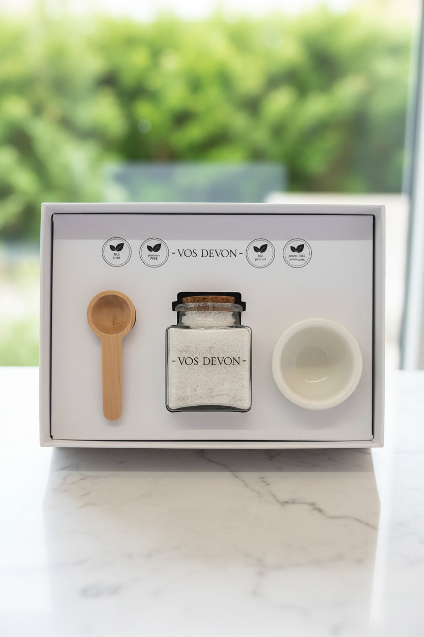 Set of VOS Devon products including a bowl, bottle with natural kaolin clay, and scoop in a box on a marble surface